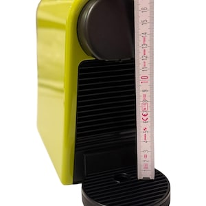 Può includere: Una macchina per caffè espresso verde lime con dettagli neri. La macchina ha una parte superiore arrotondata e un vassoio raccogli gocce nero. Un righello mostra che è alta circa 18 cm.