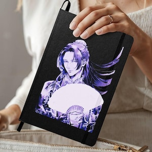 May include: Black notebook featuring a purple and white illustration of a person holding a fan. The illustration has long purple hair and is wearing a patterned robe. The notebook has a black elastic band closure and a ribbon bookmark.