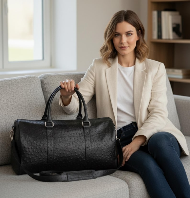 May include: A black leather duffel bag with a textured surface, featuring a top handle and a shoulder strap. The bag has silver-colored hardware and is designed for travel or overnight stays. The bag is approximately 20 inches long.