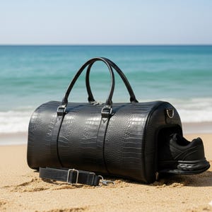 Può includere: Borsa da viaggio nera con motivo a coccodrillo, con manici superiori e tracolla staccabile. Una scarpa da ginnastica nera è visibile nello scomparto laterale. La borsa è su una spiaggia sabbiosa con l'oceano sullo sfondo.