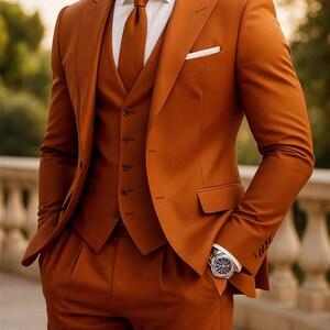 Könnte beinhalten: Ein dreiteiliger Anzug in einem warmen, gebrannten Orangeton. Der Anzug besteht aus einem Blazer mit Einstecktuch, einer Weste und einer maßgeschneiderten Hose. Ein weißes Hemd und eine passende Krawatte vervollständigen das Ensemble. Eine Armbanduhr ist sichtbar.