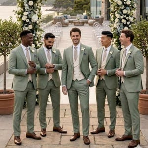 May include: Five individuals stand in a row wearing sage green suits with beige vests, white dress shirts, and beige ties. Each person wears brown leather dress shoes and a small white floral boutonniere pinned to the left lapel of their jacket.