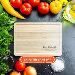 May include: A rectangular bamboo chopping board with a juice groove. The board has the text "Sam & Amelia Congratulations 18th September 2025" printed on it. Fresh vegetables surround the board.