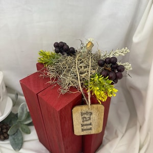 May include: A red wooden decorative box with a rustic finish, adorned with faux grapes, greenery, and a wooden tag that reads "Fall". The box is a unique autumn-themed accent piece.