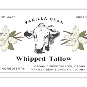 Op de afbeelding: Een wit label met zwarte tekst die "HAND MADE", "VANILLA BEAN", "ORGANIC", "Whipped Tallow", "INGREDIENTS:", "ORGANIC BEEF TALLOW, ORGANIC VANILLA BEANS, ORGANIC JOJOBA OIL" zegt. Het label heeft ook een zwart-witte illustratie van een koeienkop en twee witte vanillebloemen met groene bladeren.
