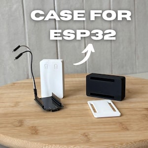 Puede incluir: Una carcasa ESP32 blanca y negra con el texto "CASE FOR ESP32". La carcasa incluye una base negra, una parte superior blanca y una pieza rectangular blanca. Una flecha apunta a la carcasa.