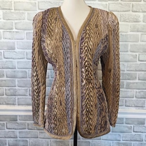 May include: A long-sleeve jacket featuring a V-neckline and a front zipper closure. The garment is constructed with vertical panels of textured, pleated fabric in alternating shades of metallic gold, bronze, and muted lavender-purple.