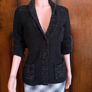 May include: Black textured jacket with a shawl collar, three buttons, and two front pockets. The jacket has three-quarter sleeves and a subtle sparkle throughout the fabric. The jacket is displayed on a mannequin.