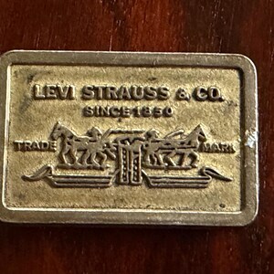 May include: A rectangular, gold-colored metal plaque with the words "LEVI STRAUSS & CO. SINCE 1850" and a graphic of two horses pulling a wagon. The words "TRADE" and "MARK" are also visible.