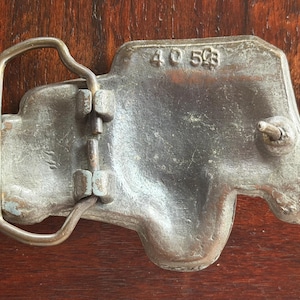 May include: A vintage metal belt buckle with a truck-shaped design. The buckle is a dull silver color with a brass-colored loop and hardware. The numbers "40 503" are stamped on the buckle.