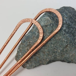 May include: Two copper hair pins with a hammered finish. The pins are bent into a U-shape at the top and are straight on the bottom.