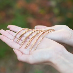 May include: A set of six gold hair pins, each with a slightly different curve, are held in the palm of a hand.