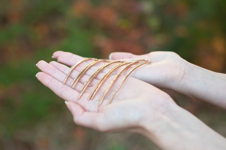 May include: A set of six gold hair pins, each with a slightly different curve, are held in the palm of a hand.