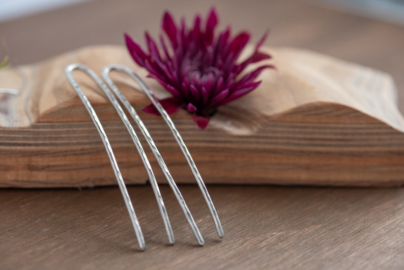 May include: Four silver hair pins with a textured surface. The pins are arranged in a row on a wooden surface.