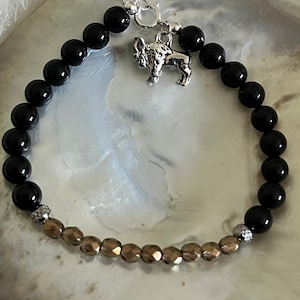 May include: A black and bronze beaded bracelet with a silver buffalo charm. The bracelet is made with round black beads and smaller, faceted bronze beads.