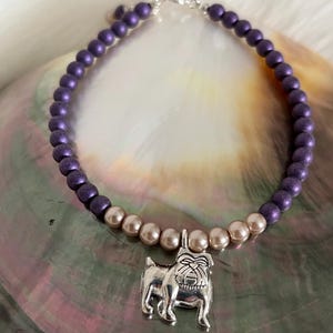 May include: Purple and beige beaded bracelet with a silver bulldog charm.