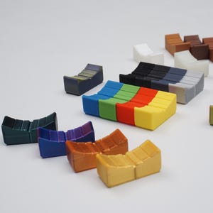 Può includere: Una collezione di oggetti colorati in miniatura a forma di gradini. Gli oggetti sono in vari colori, tra cui verde, blu, arancione, giallo e marrone. Gli oggetti sono disposti su una superficie bianca.