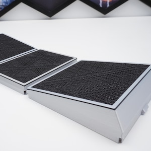 Peut inclure: Trois filtres à air rectangulaires gris avec une surface noire texturée. Les filtres ont une bordure argentée et sont disposés en rangée, légèrement inclinés vers le spectateur. Sur une surface blanche.