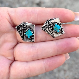 Op de afbeelding: Zilverkleurige manchetknopen in de vorm van speelkaarten met een turquoise schoppenontwerp. De manchetknopen hebben een getextureerde afwerking en een klassieke speelkaartenindeling.