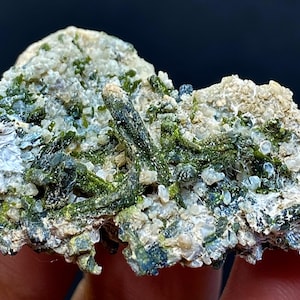 Puede incluir: Un cúmulo de cristales verdes y blancos sobre una roca. Los cristales son pequeños y tienen una textura rugosa. La roca es marrón y tiene una superficie rugosa.