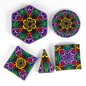 May include: Five colorful polymer clay tiles with intricate geometric designs. The tiles are in various shapes, including a hexagon, circle, square, and triangle. The designs feature a mix of bright colors, including red, orange, yellow, green, blue, purple, and black.