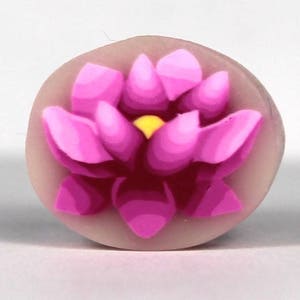 May include: A pink and white ceramic flower with a yellow center. The flower is in a raised design and looks like a lotus.