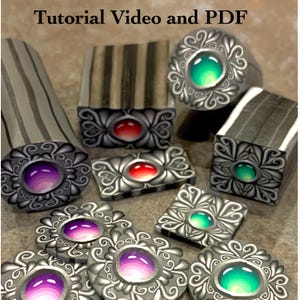 May include: A collection of handcrafted polymer clay jewelry components. The pieces feature ornate silver-toned frames with colorful, gem-like center stones in shades of purple, red, and green. The text "Tutorial Video and PDF" is visible at the top.