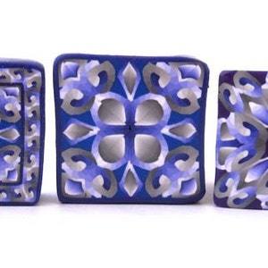 K&ouml;nnte beinhalten: Drei quadratische Keramikfliesen mit komplizierten geometrischen Mustern in Blau, Lila und Grau.