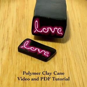 Könnte beinhalten: Zwei Polymer-Ton-Stücke mit dem Wort "love" in weißer Schrift, umrandet in Pink, auf schwarzem Hintergrund. Ein Stück ist ein rechteckiger Block, das andere ein kleinerer, rechteckiger Schnitt. Auf einer Holzoberfläche.