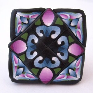 K&ouml;nnte beinhalten: Eine geometrische Fliese in Schwarz, Gr&uuml;n, Blau und Rosa mit einem sich wiederholenden Muster. Die Fliese ist aus Polymer Clay gefertigt und hat eine gl&auml;nzende Oberfl&auml;che.