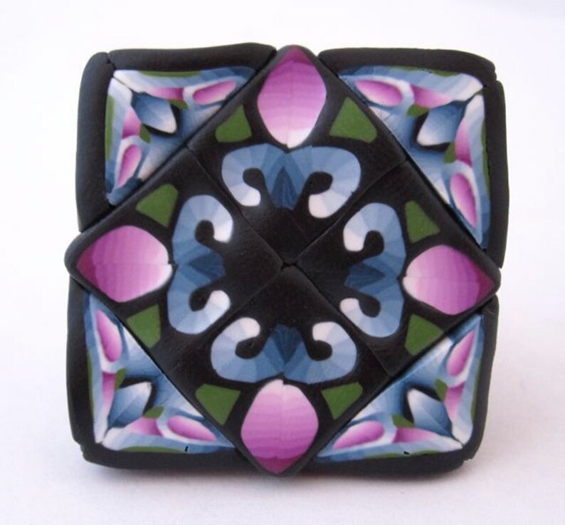 K&ouml;nnte beinhalten: Eine geometrische Fliese in Schwarz, Gr&uuml;n, Blau und Rosa mit einem sich wiederholenden Muster. Die Fliese ist aus Polymer Clay gefertigt und hat eine gl&auml;nzende Oberfl&auml;che.