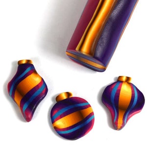 Puede incluir: Tres adornos navideños hechos a mano con forma de lágrima. Los adornos están hechos de arcilla polimérica y presentan un patrón de espiral de morado, dorado y azul.