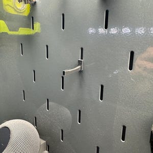 May include: A gray pegboard with a black metal hook and a gray speaker attached to it.