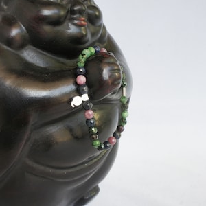 May include: A beaded bracelet with green, blue, and pink stones. The bracelet is wrapped around the arm of a black ceramic statue.