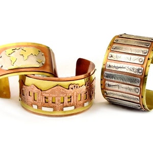 May include: Three metal bracelets with different designs. The first bracelet features a world map, the second bracelet features a building, and the third bracelet features a striped pattern.