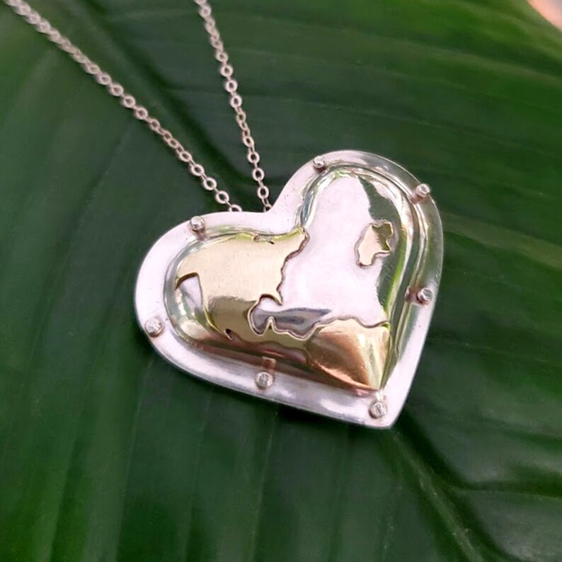 Puede incluir: Un collar con un colgante en forma de coraz&oacute;n de plata con un interior dorado. El colgante presenta un dise&ntilde;o texturizado y est&aacute; acentuado con peque&ntilde;os puntos plateados alrededor de los bordes.