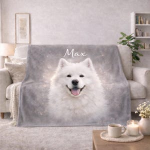 May include: A gray plush blanket featuring a smiling white Samoyed dog with the name "Max" in white script. The blanket is draped over a light-colored sofa. A coffee table with a cup, candle, and vase is in front.
