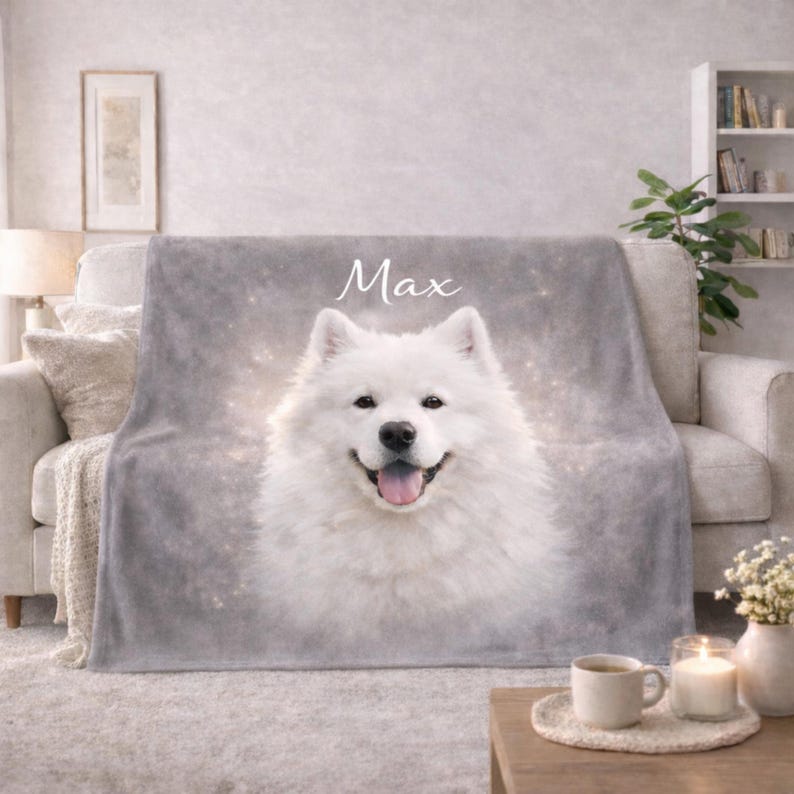 May include: A gray plush blanket featuring a smiling white Samoyed dog with the name "Max" in white script. The blanket is draped over a light-colored sofa. A coffee table with a cup, candle, and vase is in front.