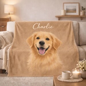 May include: A tan throw blanket featuring a smiling golden retriever dog portrait with the name "Charlie" in script. The blanket is draped over a sofa. A coffee table holds a mug, candle, and small vase.