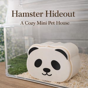K&ouml;nnte beinhalten: Ein klarer Hamsterk&auml;fig aus Kunststoff mit einem wei&szlig;en, panda-f&ouml;rmigen Versteck. Das Versteck hat schwarze Ohren und Augen sowie einen l&auml;chelnden Mund. Der Text "Hamster Hideout" und "A Cozy Mini Pet House" sind zu sehen.