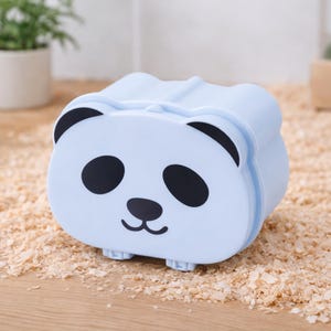 K&ouml;nnte beinhalten: Ein hellblaues Panda-f&ouml;rmiges Beh&auml;ltnis mit schwarzen Augen, Ohren und Nase. Der Beh&auml;lter hat eine rechteckige Form mit abgerundeten Kanten und kleinen F&uuml;&szlig;en. Der Hintergrund ist eine Holzoberfl&auml;che mit Holzsp&auml;nen.