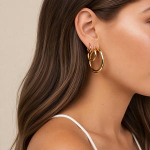 May include: A set of three gold hoop earrings of varying sizes worn in a single ear. The earrings feature a smooth, polished, circular design with a reflective metallic finish. The hoops are graduated in size, with the largest at the bottom.