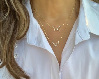 May include: A layered gold necklace set featuring two delicate chains. Each chain holds a small, horizontal pendant shaped like a star constellation, accented with tiny, clear, round-cut stones that mimic the appearance of sparkling stars.