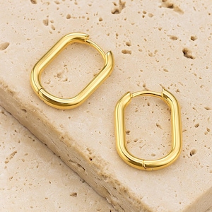 May include: Two gold-colored, rectangular hoop earrings. The earrings are displayed on a textured, light beige surface. The earrings have a polished finish and a simple, modern design. The brand name "Mythos Aurum" is visible in the bottom right corner.
