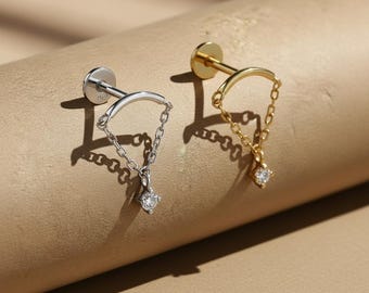 Peut inclure: Deux boucles d'oreilles à clous, une argentée et une dorée, chacune avec un motif de chaîne et une pierre précieuse ronde et transparente. Les boucles d'oreilles ont un dos plat et circulaire. Elles sont présentées sur une surface neutre et texturée.