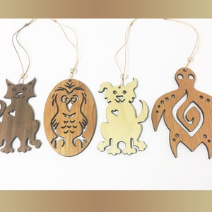 Può includere: Quattro ornamenti in legno, ognuno con un animale diverso: un gatto, un gufo, un cane e una tartaruga. Gli ornamenti sono tutti marroni e hanno una finitura in legno naturale. Sono appesi a uno spago.