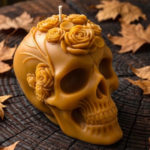 May include: A golden yellow beeswax candle shaped like a human skull, featuring intricate molded rose floral details on the top and side. A single white cotton wick protrudes from the center of the floral arrangement on the crown of the skull.