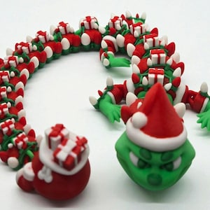 May include: A whimsical Christmas-themed display featuring a green character wearing a Santa hat, a red sack of gifts, and a decorative garland of red, white, and green elements. The garland is shaped like a snake, with small gift boxes.