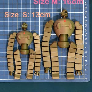 K&ouml;nnte beinhalten: Zwei zerlegte Roboter-Spielzeuge, eines braun und eines gr&uuml;n, mit segmentierten Gliedma&szlig;en. Der gr&ouml;&szlig;ere Roboter ist 16 cm gro&szlig; und der kleinere 13 cm.  Gr&ouml;&szlig;e S: 13 cm Gr&ouml;&szlig;e M: 16 cm