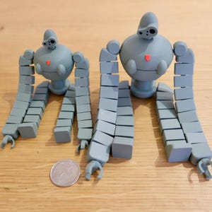 K&ouml;nnte beinhalten: Zwei graue, artikulierte Roboter-Spielzeuge mit segmentierten Gliedma&szlig;en. Der gr&ouml;&szlig;ere Roboter ist etwa doppelt so gro&szlig; wie der kleinere.